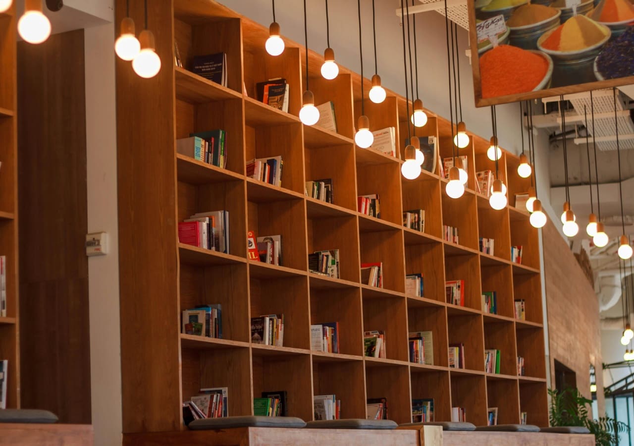 A bookshelf with many books on it and lights hanging from the ceiling.